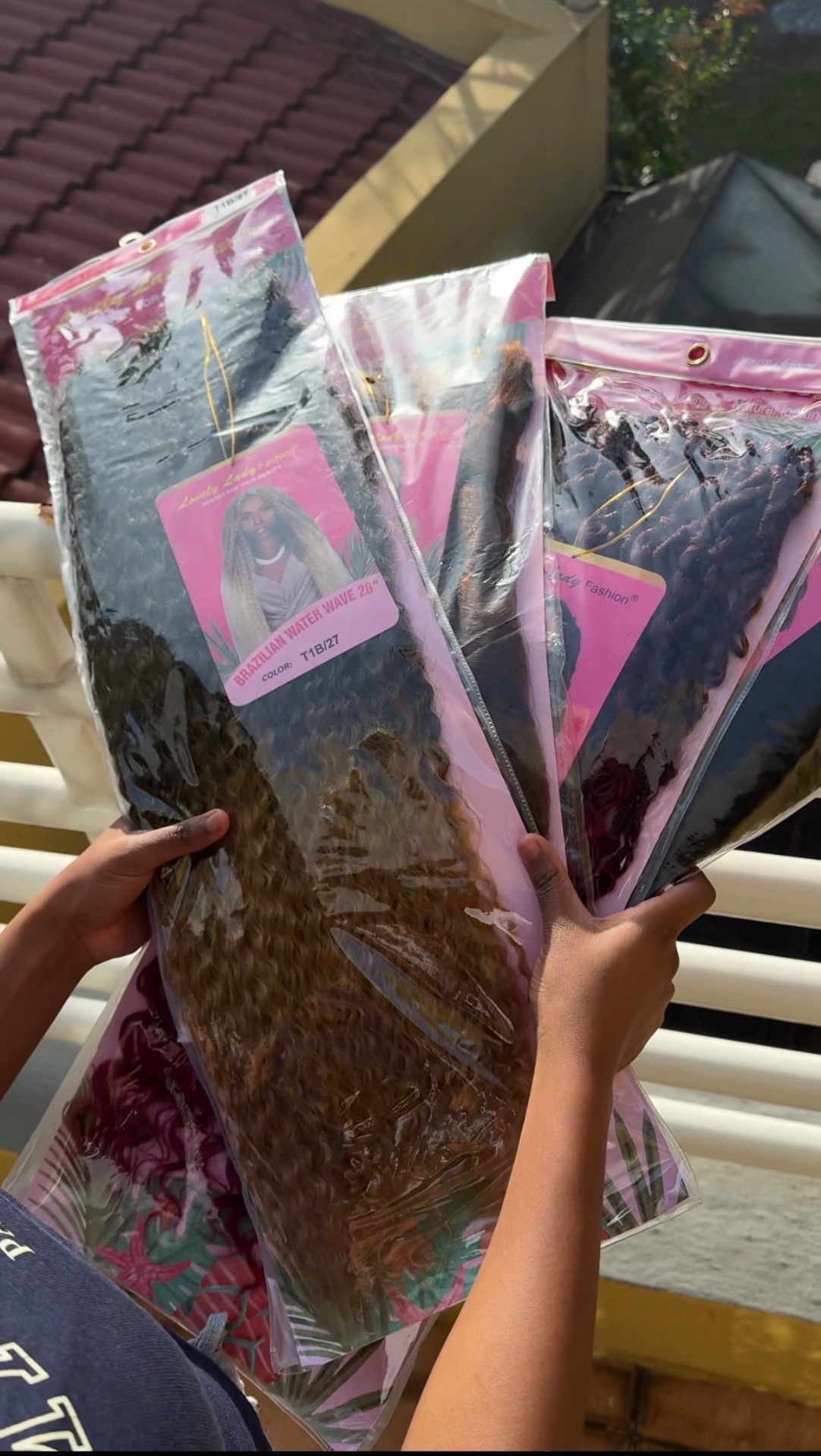 Hands holding three packs of Lovely Lady Fashion Brazilian Water Wave hair outdoors